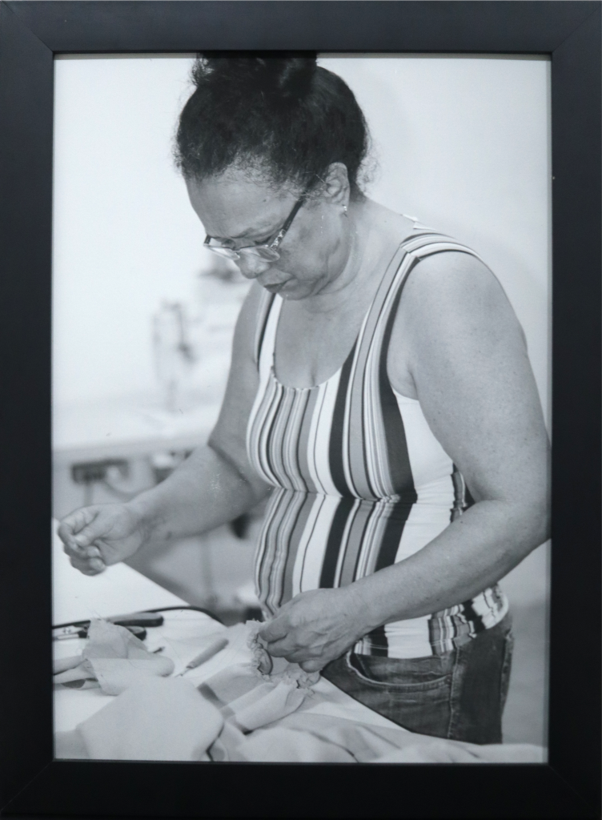 Memória Individual | 2024 | Fotografia | 29,7 cm x 42,0 cm 

É apresentada em seu gesto de trabalho, concentrada no manejo do tecido, revelando a força silenciosa de quem constrói, repara e sustenta a vida pelas mãos. A fotografia em preto e branco intensifica a memória, a intimidade e a dignidade da cena, valorizando o ofício, e a presença feminina como base de afeto e reconhece a potência das mulheres amazônicas, que transformam necessidade em criação, cuidado em sustento e trabalho em gesto de amor.